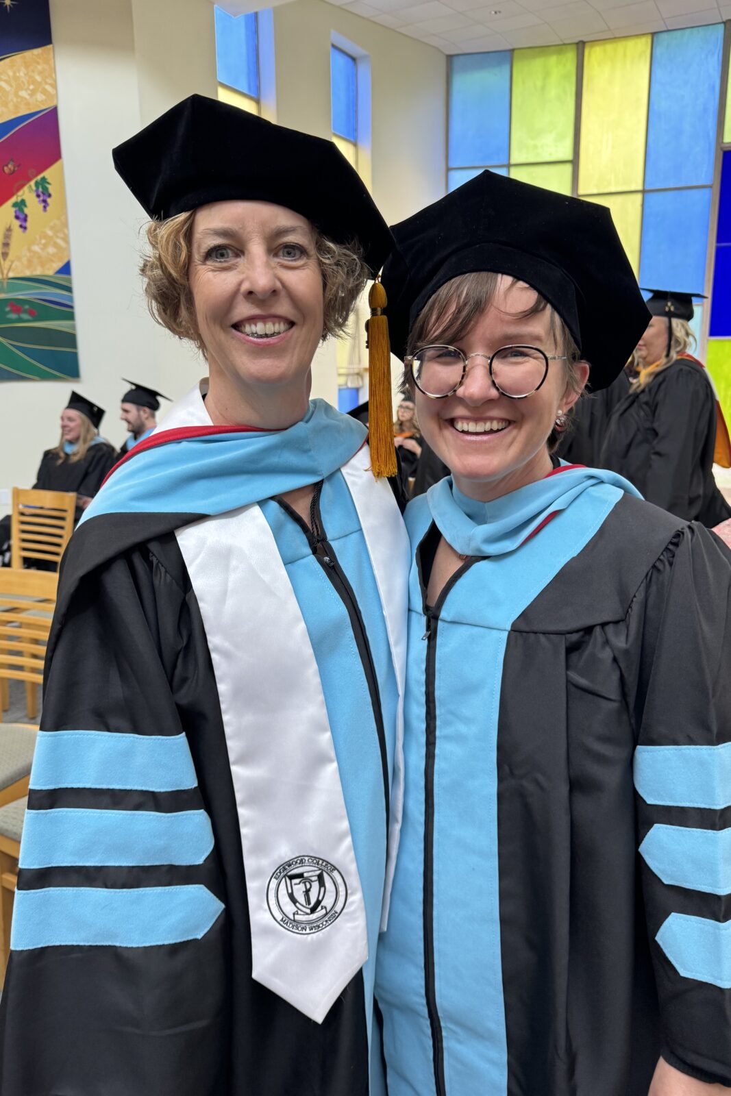 2 women smiling next to each other in graduation gowns